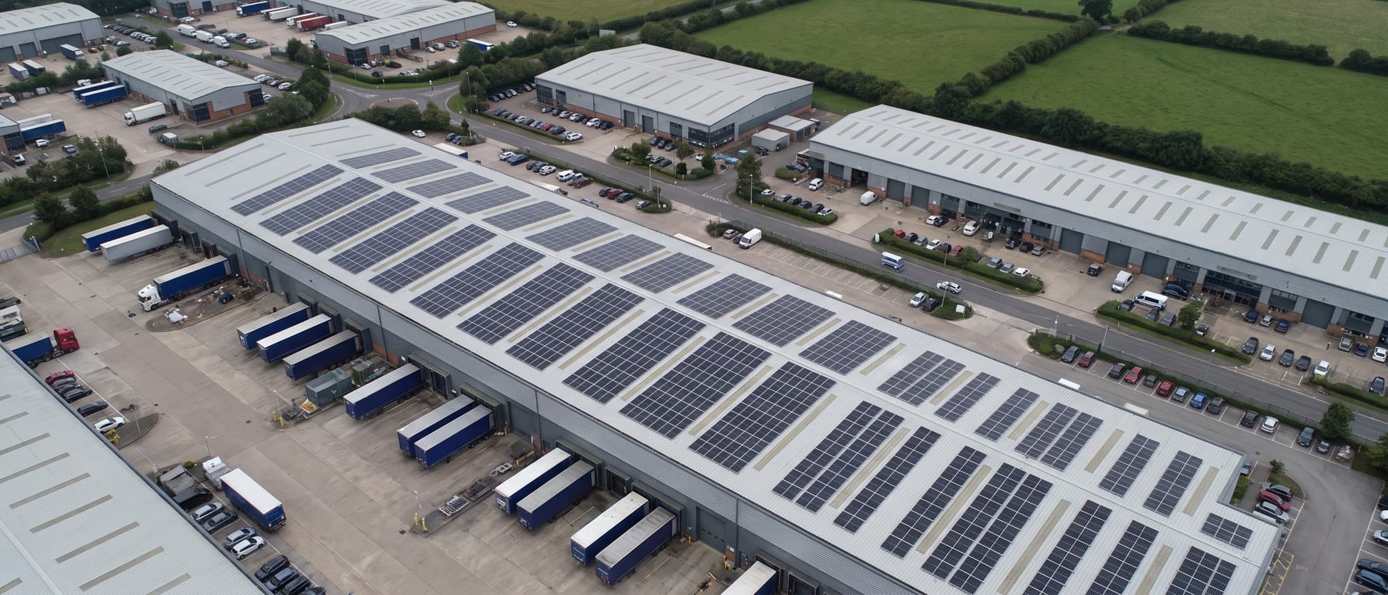 Aerial view of a UK industrial estate where several commercial roofs carry solar arrays and others are still bare.